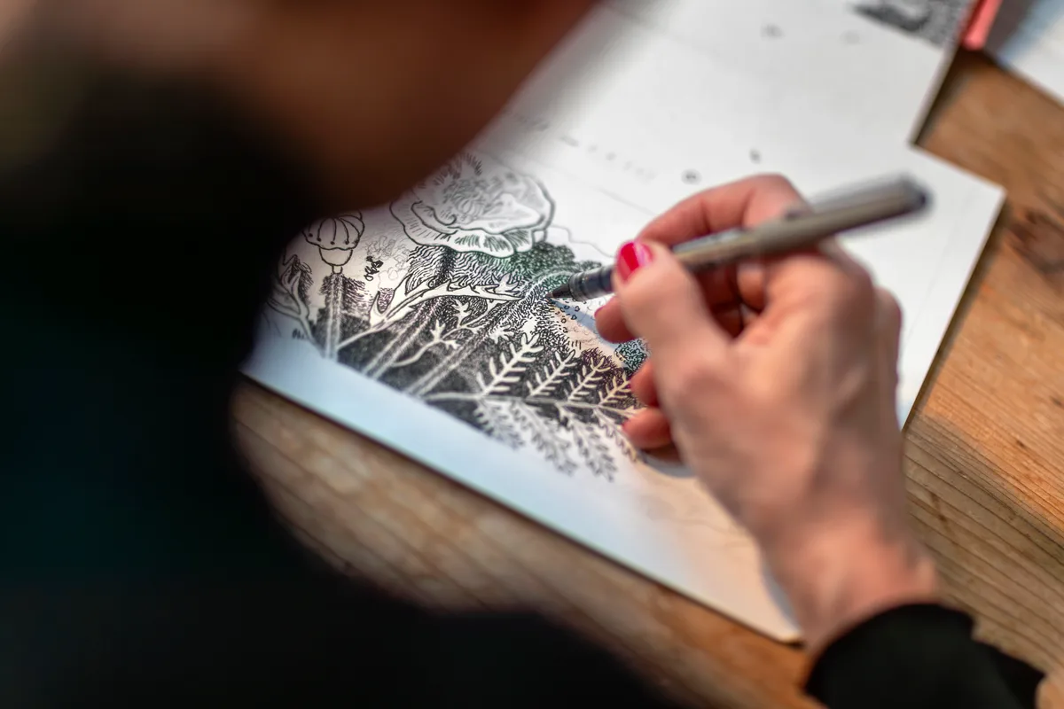 Die Künstlerin hält einen Stift in der rechten Hand und zeichnet eine Skizze.